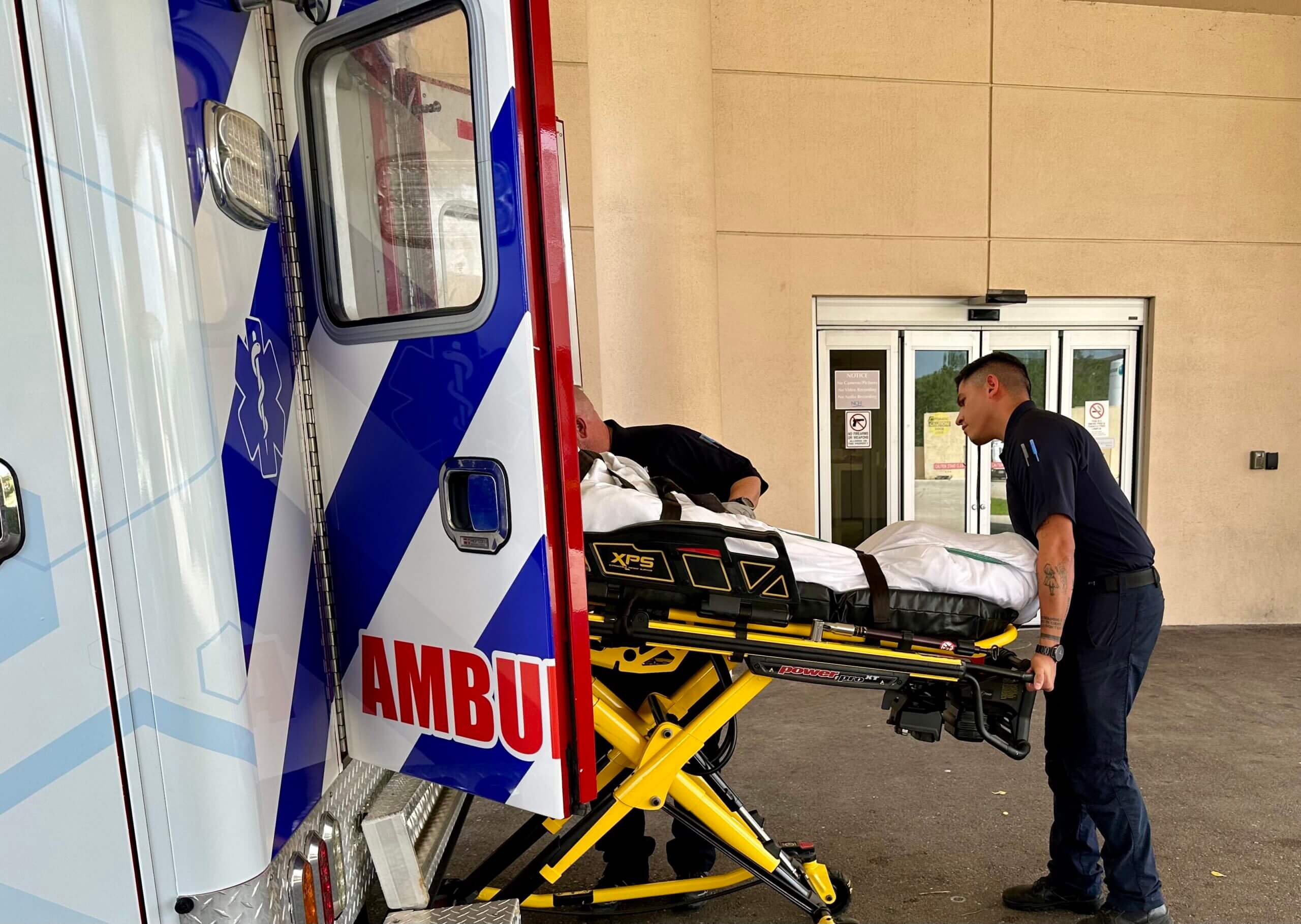 A person loading a person on a stretcher to an ambulance.
